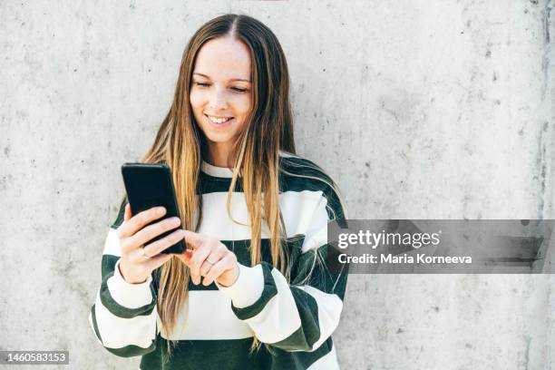 young woman using smartphone against gray wall. - pick tooth photos et images de collection