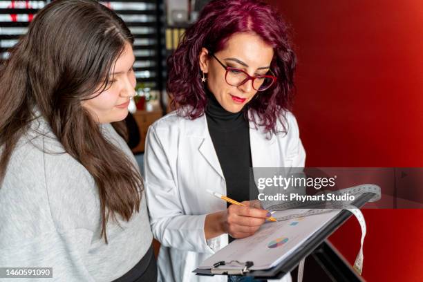 female nutritionist gives consultation to teenager patient indoors in the office - young chubby girl stock pictures, royalty-free photos & images
