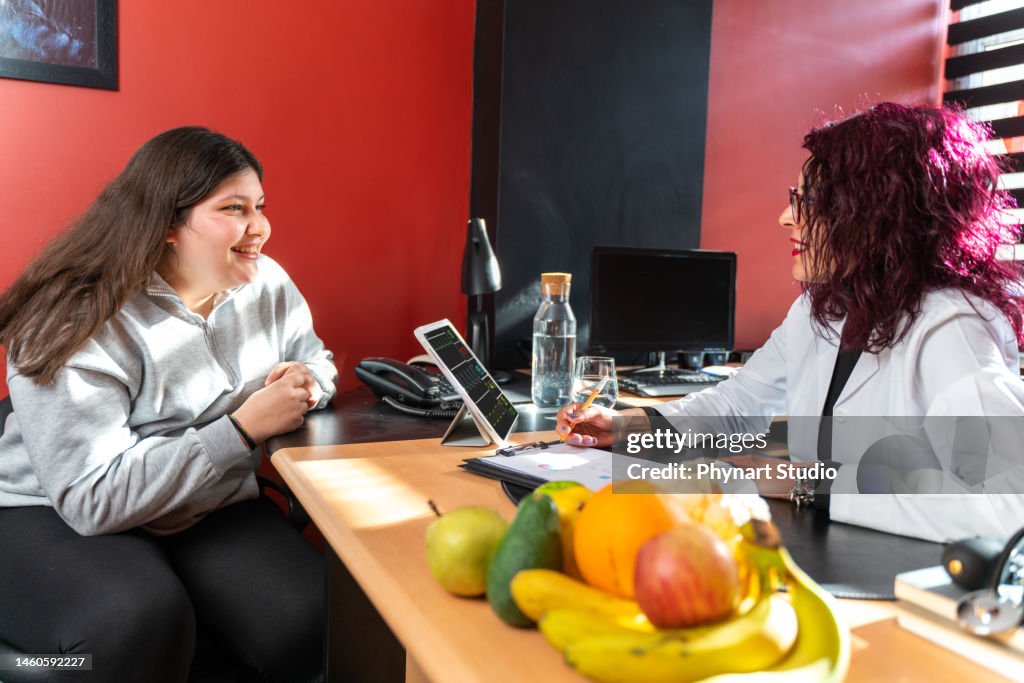 Female nutritionist with digital tablet gives consultation to teenager patient indoors in the office