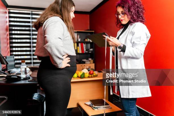 ernährungswissenschaftler untersucht die taille eines teenagermädchens mit einem maßband, um klinische ernährung zu verschreiben - fat hips stock-fotos und bilder