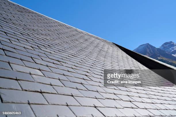 slate shingle roof on the exterior of a house seen from a low angle on a sunny day with a clear sky - damaged shingles stock pictures, royalty-free photos & images