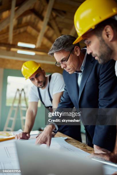 architect and manual workers examining blueprints at construction site. - real estate developer stock pictures, royalty-free photos & images