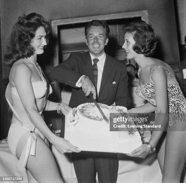 British comic actor Brian Rix cutting a cake held by two women named as Jackie Fleming and Sherrie Ann Scott, on September 15th, 1959.