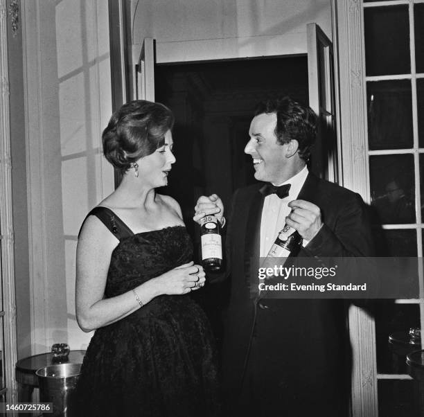 British comedy actor Brian Rix and wife Elspet Gray pictured with wine bottles at an event on January 30th, 1961.