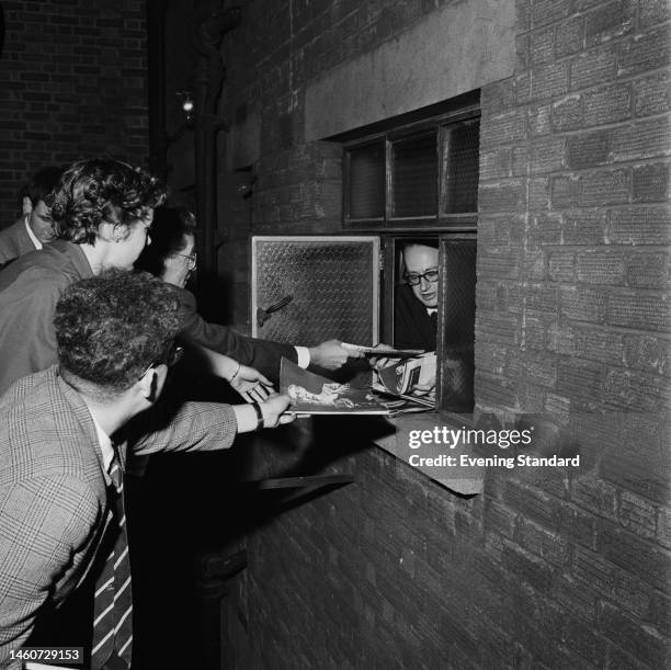American jazz saxophonist Paul Desmond of the Dave Brubeck Quartet signs autographs for fans waiting outside his dressing room window at a London...