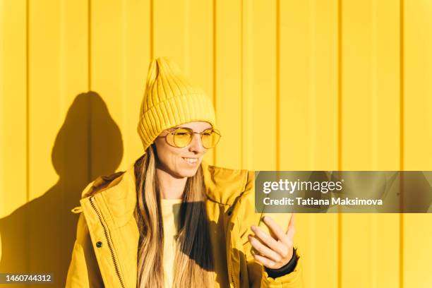 young woman in yellow hat, jacket and yellow glasses with yellow phone. - monocromo vestimenta fotografías e imágenes de stock