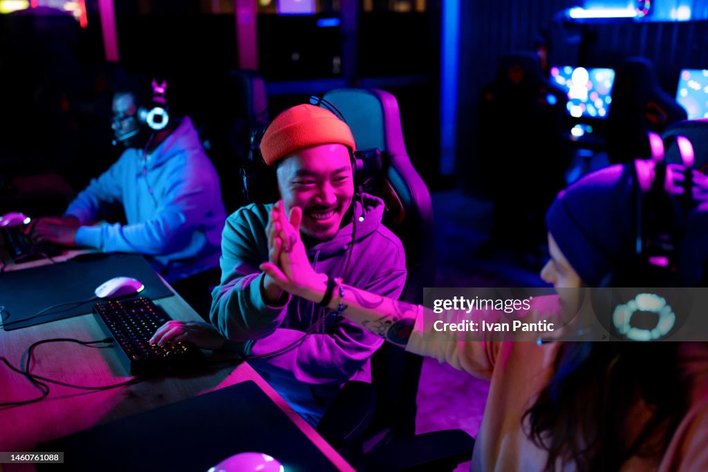 Happy Asian gamer congratulating his friend on winning in eSports.