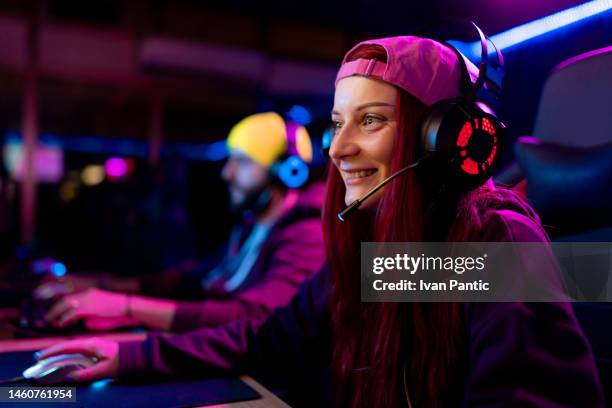 happy female gamer with headset playing video games in entertainment club. - esports stock pictures, royalty-free photos & images