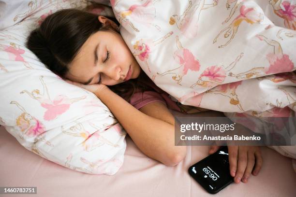sleeping teenage girl, covered with pink blanket, holding mobile phone - alarm clock stock-fotos und bilder
