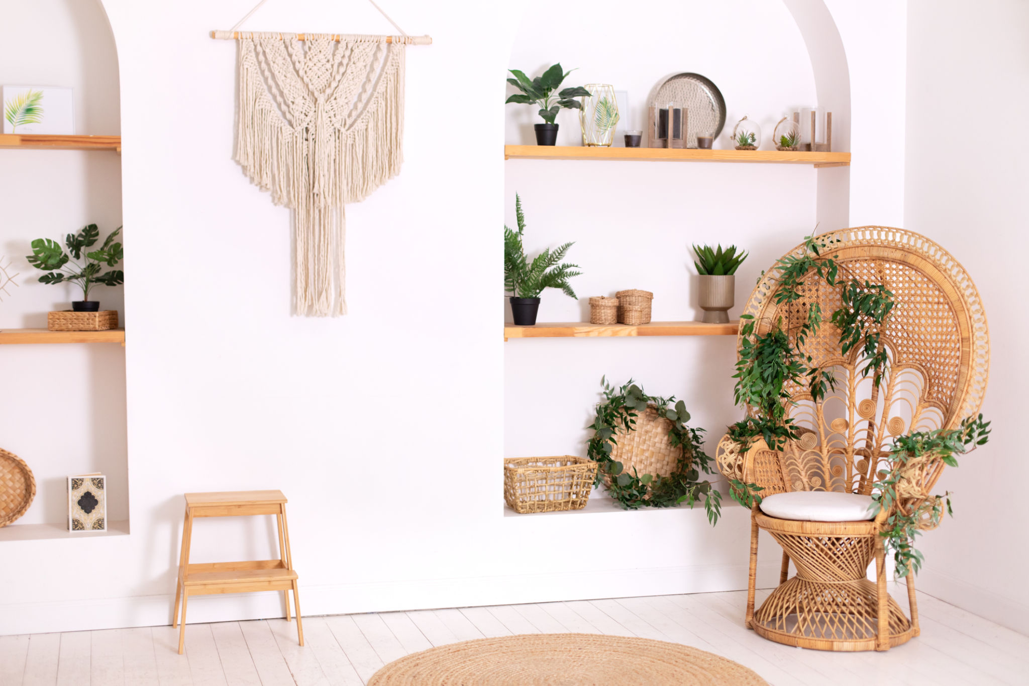 Rattan peacock armchair by the white wall in the living room. Wabi sabi room interior. Eco natural furniture. Design peacock wicker chair and wooden shelfs with decor in stylish bedroom interior. Rattan peacock armchair by the white wall in the living room. Wabi sabi room interior. Eco natural furniture. Design peacock wicker chair and wooden shelfs with decor in stylish bedroom interior.