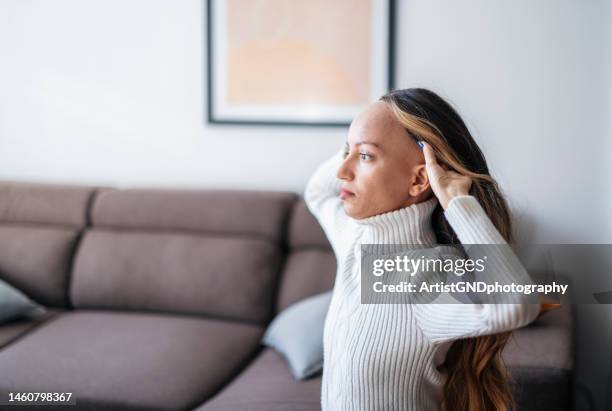 shot of a young woman with cancer putting on a wig. - toupee stock pictures, royalty-free photos & images