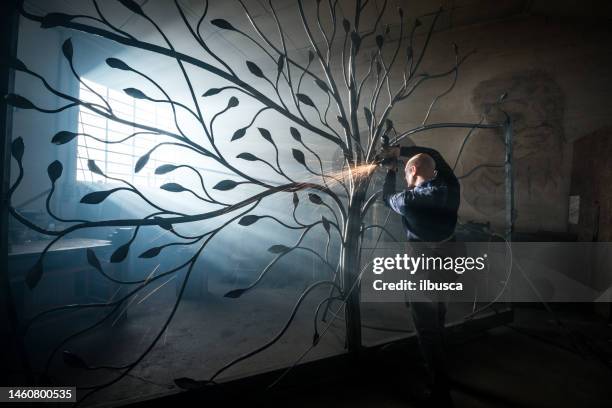 blacksmith artist working in his smithy studio creating a gate-tree - smederij stockfoto's en -beelden