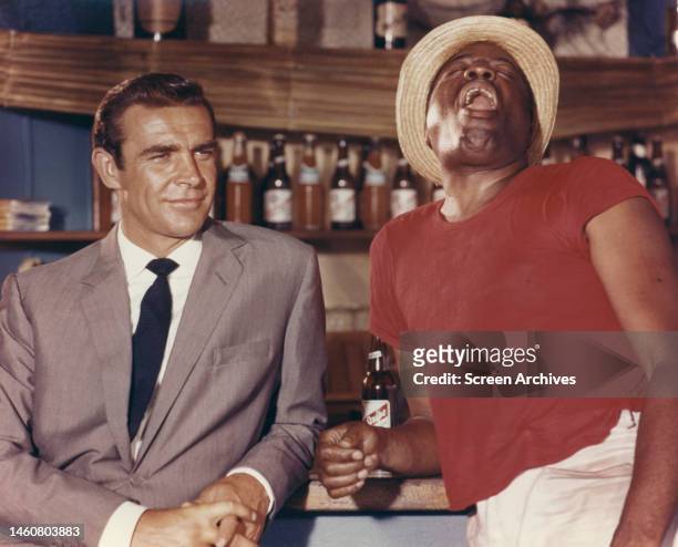 'Dr No' 1962 Sean Connery as James Bond 007 with John Kitzmiller as Quarrel standing by bar in the Bahamas.