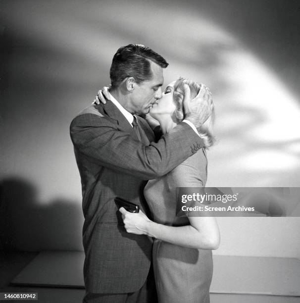 Eva Marie Saint holding a pistol to Cary Grant while kissing him, in a promotional still for the 1959 Alfred Hitchcock thriller, 'North By Northwest'.