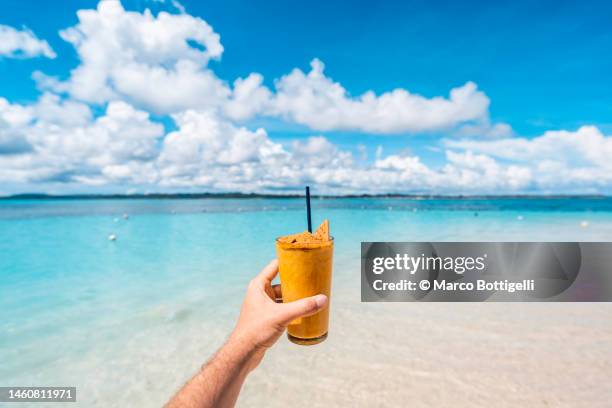 personal perspective of man drinking a mango graham shake on tropical beach - mango smoothie stock pictures, royalty-free photos & images