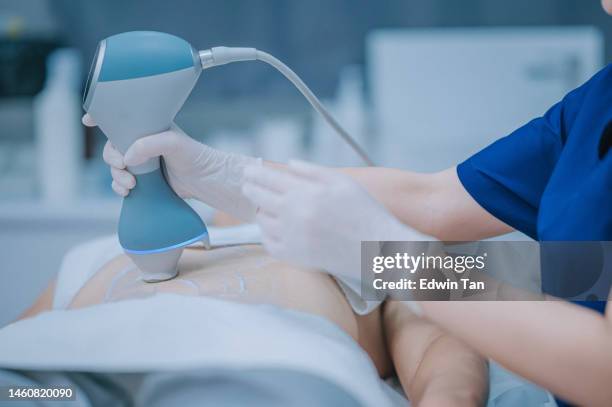 asian chinese female aesthetician ultrasound abdominal fat and cellulite removal. body care, spa treatment for her client - tighten stock pictures, royalty-free photos & images