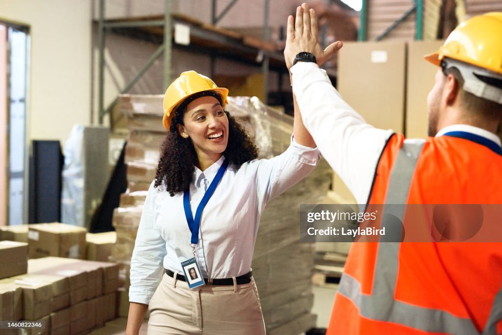 Man, woman and high five in warehouse for logistics, shipping and product transport with safety, ppe and happy. Teamwork, factory staff and motivation with smile, helmet and box for transportation