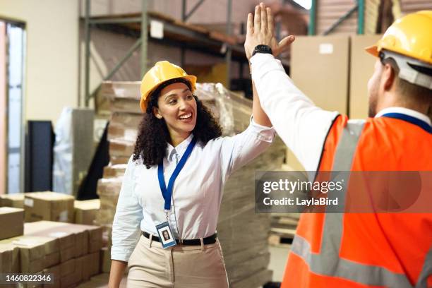 man, woman and high five in warehouse for logistics, shipping and product transport with safety, ppe and happy. teamwork, factory staff and motivation with smile, helmet and box for transportation - high five stock pictures, royalty-free photos & images