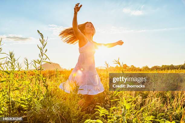 attraktive junge frau tanzt bei sonnenuntergang auf einer wiese - sommerkleid stock-fotos und bilder