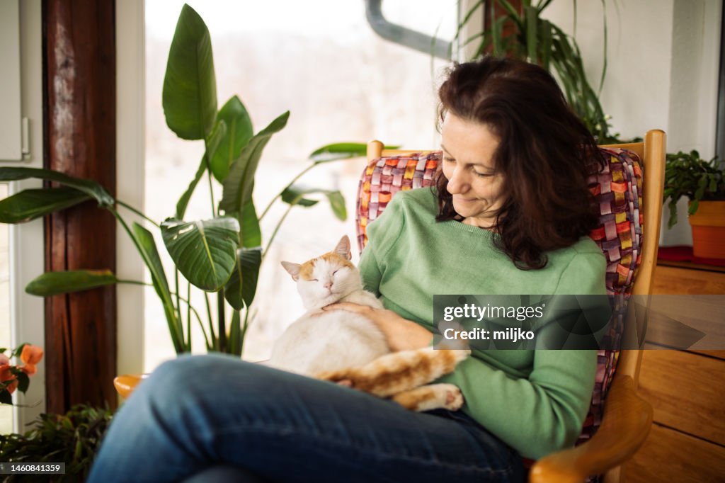 Woman sitting on her terrace and holding beautiful cat in her lap