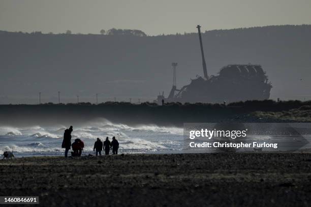 People walk on the beach at Seaton Carew as the recently demolished Redcar steel blast furnace lists forlornly on January 30, 2023 in Hartlepool,...