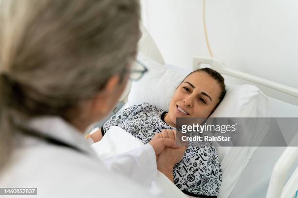 female senior doctor checking on a hospitalized young patient lying down on bed - patient lying down stock pictures, royalty-free photos & images