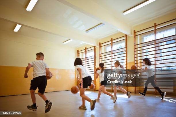 schulkinder üben das dribbling während des sportunterrichts - kind im grundschulalter stock-fotos und bilder