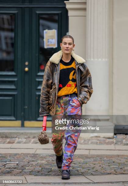 Model Vera van Erp wears brown washed out shearling leather jacket, orange black jumper, red purple green camouflage pants, Ganni bag, black boots...