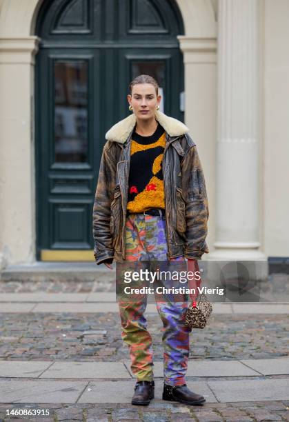 Model Vera van Erp wears brown washed out shearling leather jacket, orange black jumper, red purple green camouflage pants, Ganni bag, black boots...