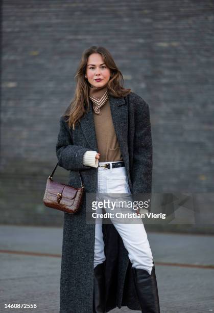 Therese Hellström wears white pants, black knee high boots, grey coat, burgundy bag, brown scarf, jumper outside Herskind during the Copenhagen...