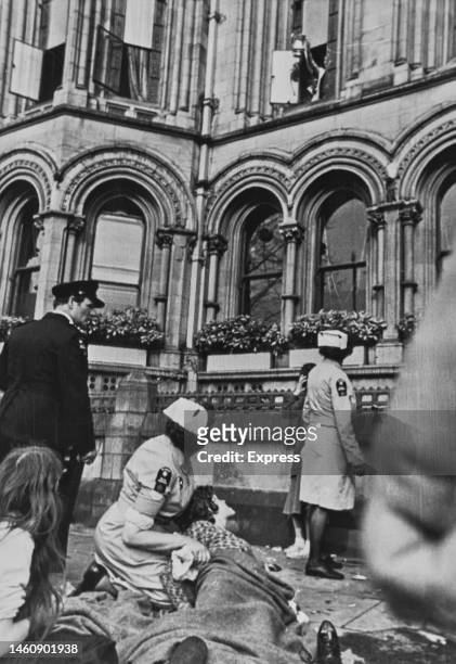 The FA Cup is brandished out of a Manchester Town Hall window while nurses care for an injured young football fan on the pavement below after...