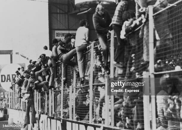 Football fans climbing over a wire fence to escape the crush on the stadium terraces at a Manchester United game, other fans are seen pressed against...