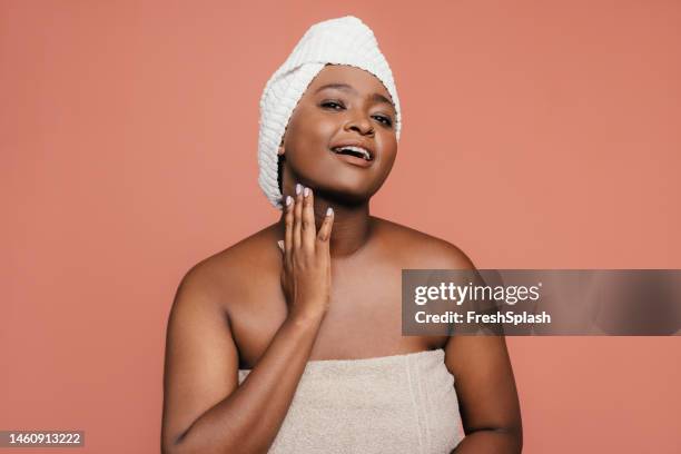 a happy beautiful woman wrapped in a towel looking at camera while taking care of her skin - wet face stock pictures, royalty-free photos & images