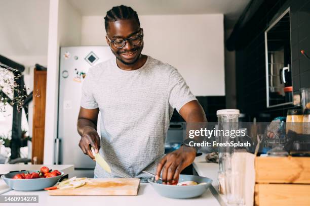 a happy man with glasses preparing healthy breakfast while standing in the kitchen - black cook stockfoto's en -beelden