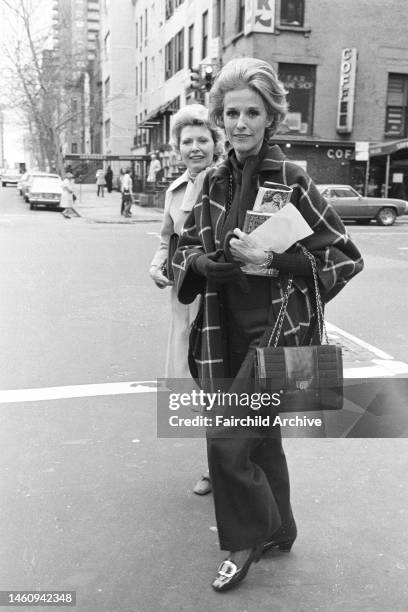 Socialite Babe Paley wearing signiture slacks and carrying a Chanel bag while wearing seasonally chic knit gloves and sporting a large plaid jacket,...