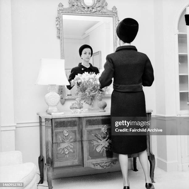 Gloria Guinness fastening her buttons in her suite in the Waldorf Towers wearing a black wool Givenchy jacket bordered in black faille over a...