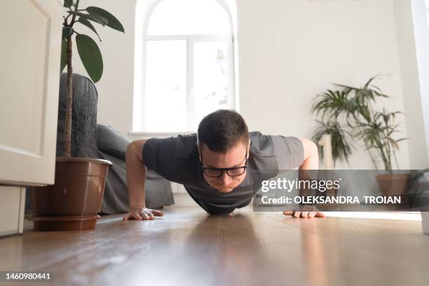 front view of mid adult man doing clapping push-ups at home. - flexiones fotografías e imágenes de stock
