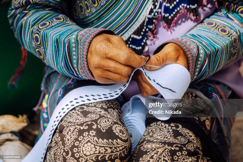 Vietnamese Hmong woman busy at sewing colorful traditional fabric