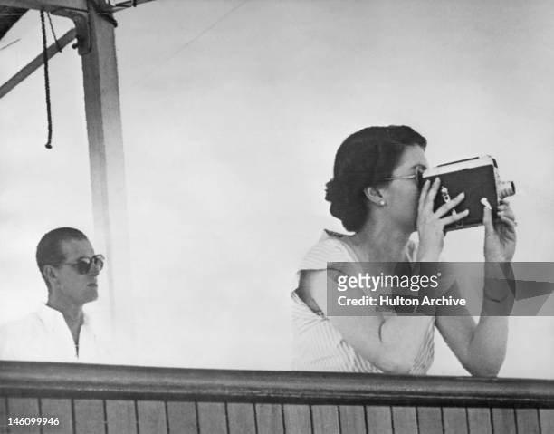 Queen Elizabeth II filming the arrival of the escort ship HMNZS Black Prince, while in the South Pacific en route to Fiji, aboard the SS Gothic...