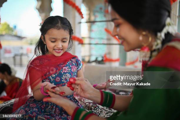 cute girl smiling at her mother while she applies alta (red dye) on her hands during a traditional function - bracelet festival stock-fotos und bilder