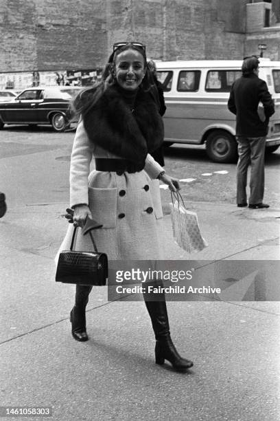 Lyn Revson, wife of Revlon's Charles Revson, wearing a double-breasted boucle wool coat with a heavy fur collar, knee-high boots and a quilted Chanel...