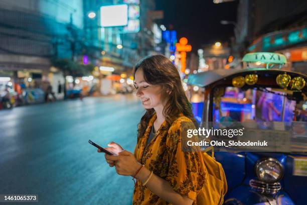 woman with smartphone standing near tuk-tuk  in chinatown in bangkok - sabbatical stockfoto's en -beelden