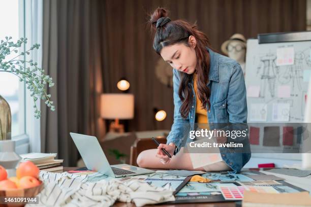 new work consulting on smartphone asian adult female woman fashion designer cloth tailor working for new collection sketch drawing choosing new color swatch fabric sample at her desk in her design studio home studio - art and craft stock pictures, royalty-free photos & images