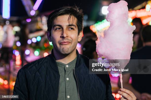 young man eating cotton candy on a night out at the amusement park. - indulgence fotografías e imágenes de stock