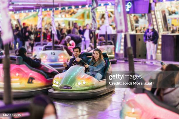 smiling friends driving bumper cars at the amusement park at night. - fairground ride stock pictures, royalty-free photos & images