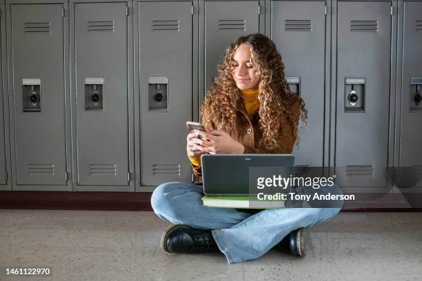 female student in high school hallway using laptop and phone - student girl using laptop computer and smart phone stock-fotos und bilder