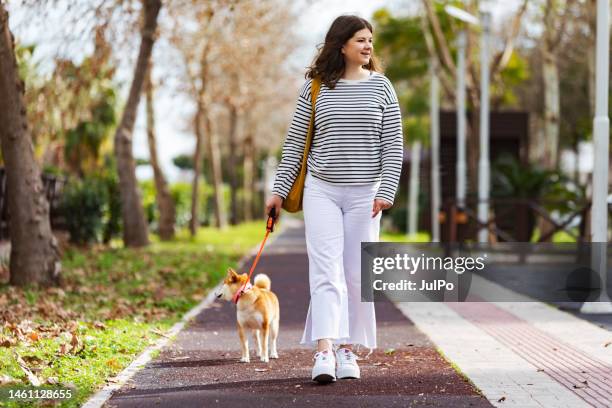 young woman walking in park with her shiba inu dog - shiba inu adult stock pictures, royalty-free photos & images