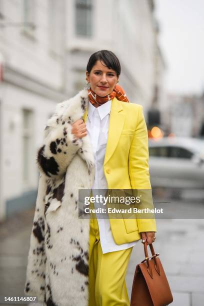 Gili Biegun wears gold earrings, a camel and white striped print pattern silk scarf, a white shirt, a pale yellow blazer jacket, matching pale yellow...