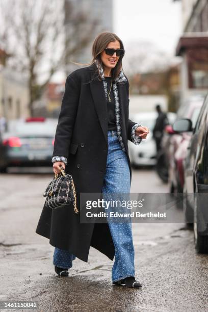 Darja Barannik wears black and burgundy print pattern sunglasses, a gold chain with logo pendant necklace from Chanel, a black t-shirt, a black wool...