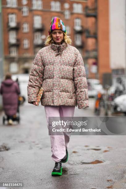 Guest wears a multicolored braided striped print pattern wool beanie, a beige with red and gray flower print pattern high neck puffer jacket from...